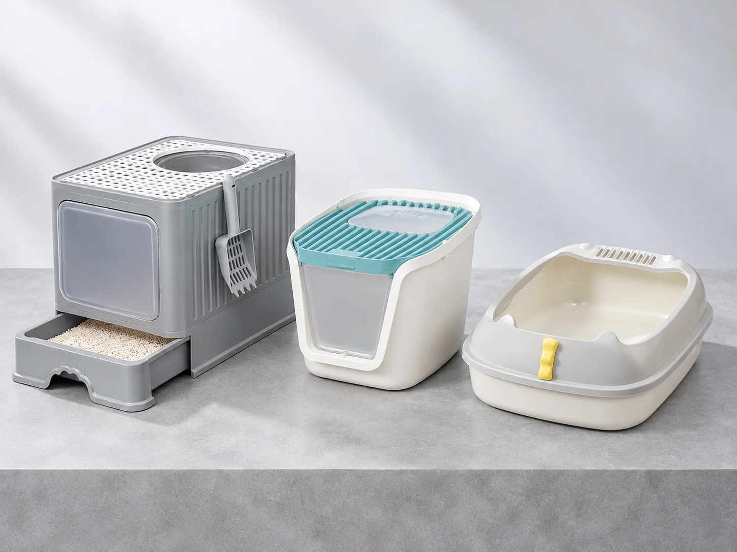Grey cat litter box with bottom pull-out drawer and round top opening, white-and-blue lidded box and cream open-front litter pan