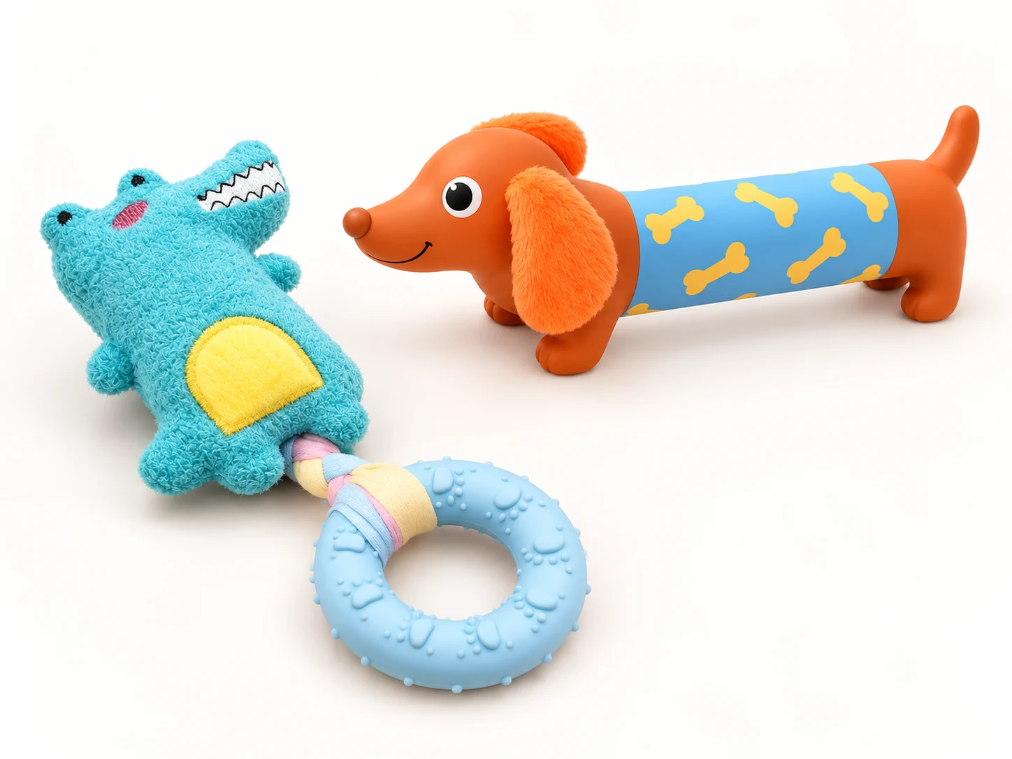 Blue plush crocodile dog toy, orange dachshund toy and blue textured dog chew ring on a white background