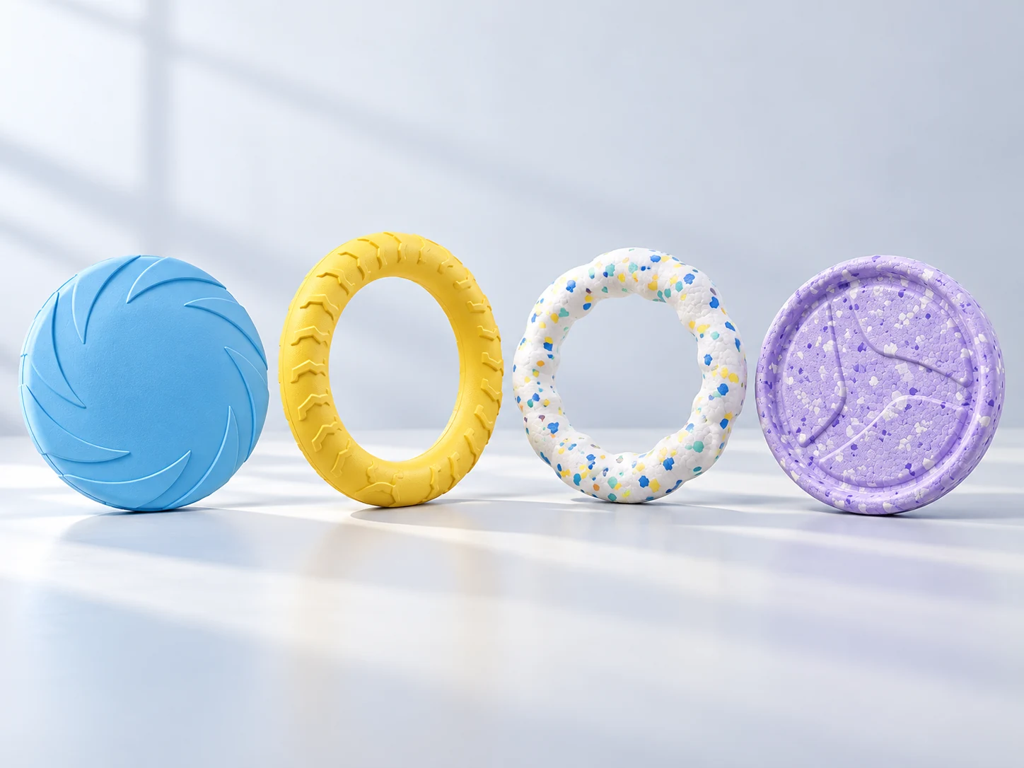 Four moulded dog fetch toys: blue patterned flying disc, yellow textured ring, white speckled ring and lavender speckled circular disc