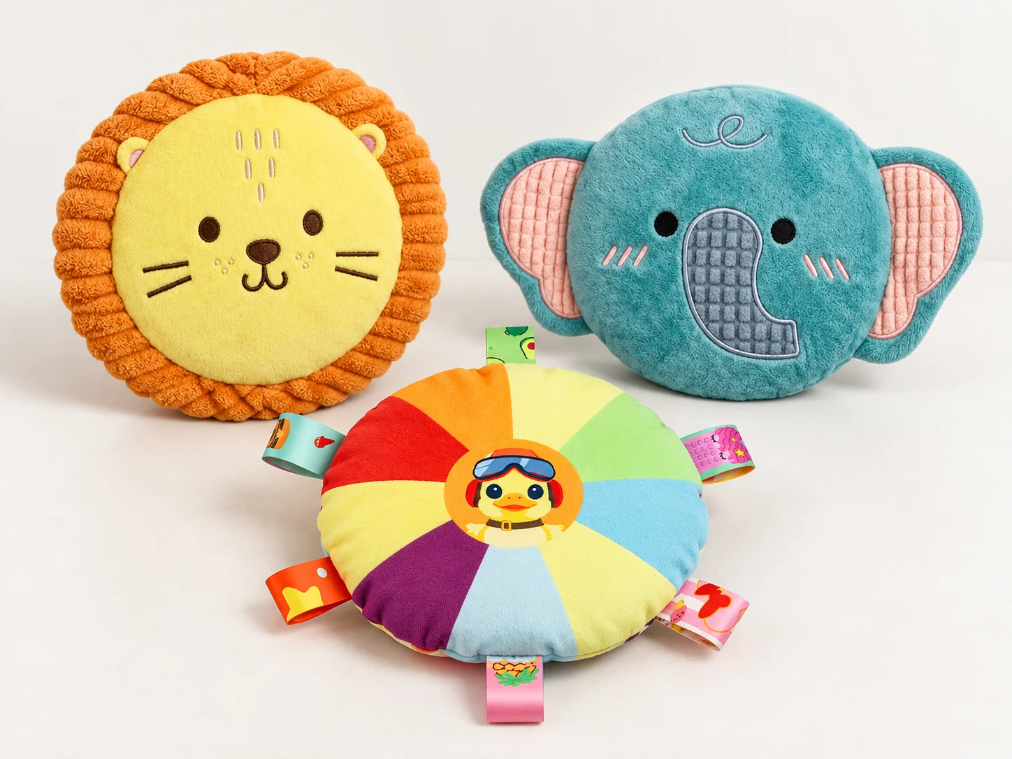 Lion and elephant plush dog flying disc toys beside a round multicoloured fabric dog fetch toy with ribbon tabs