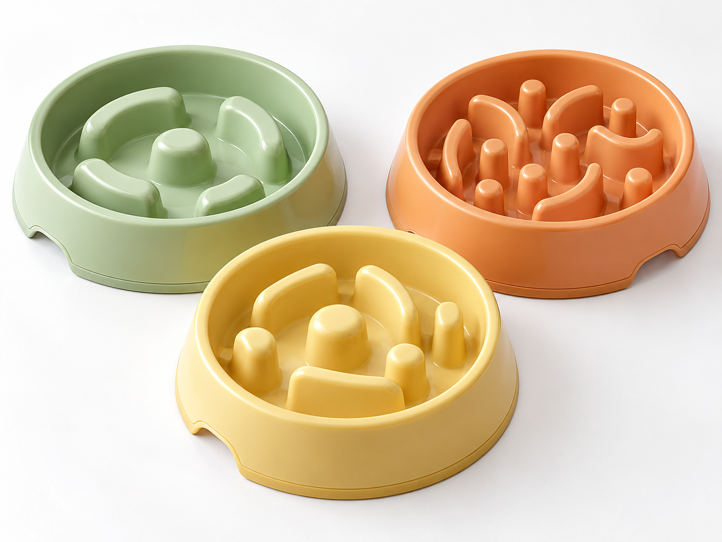 Green, orange and yellow plastic pet slow feeder bowls with different raised feeding layouts.