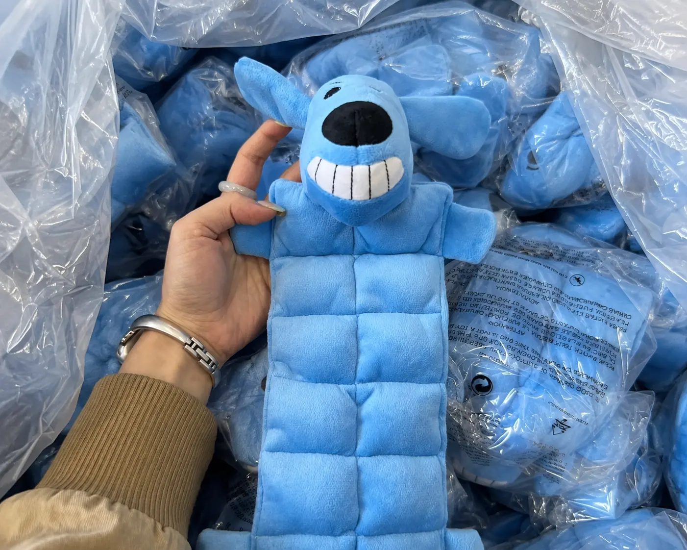 Blue dog-shaped plush toy sample held beside a batch of matching toys.
